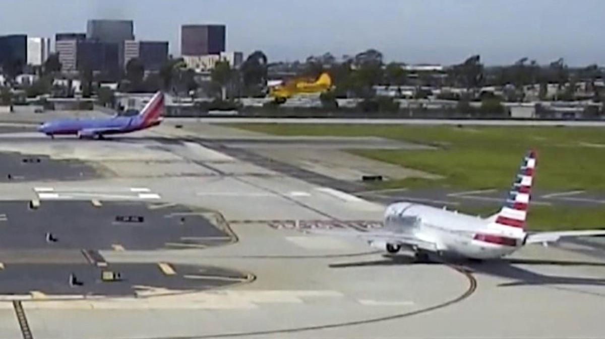 In this Feb. 13, 2017, image from video provided by John Wayne Airport, actor Harrison Ford piloting an Aviat Husky, yellow plane at center, passes low over an airliner, bottom right, before he mistakenly landed on a taxiway at John Wayne Airport in Santa Ana, Calif.