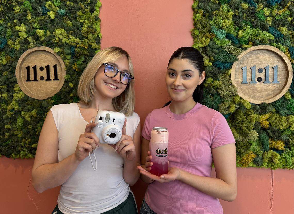 Baristas Madeline May, left, and Zahrah Alsheikh post in front of the selfie wall at 11:11 Coquetry Maison, a new coffee shop that’s open late each night at Douglas and Emporia.