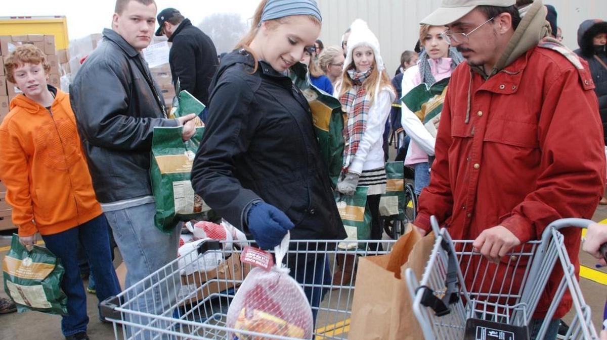 Volunteer Melissa Stoltz, center, drops a turkey in a customer’s cart during a Bread of Life Thanksgiving food distribution.