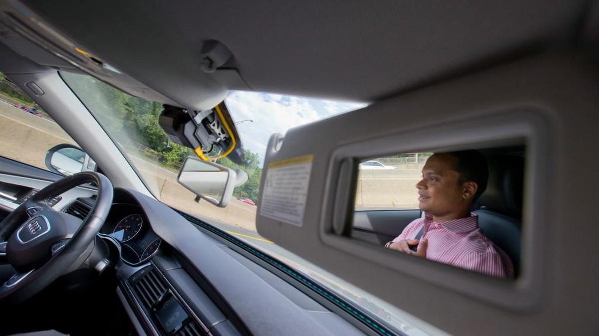 Kaushik Raghu, senior staff engineer at Audi, is reflected in the passenger-side visor mirror while demonstrating an Audi self-driving vehicle on I-395 expressway in Arlington, Va., on Friday. Experts say the development of self-driving cars over the coming decade depends on an unreliable assumption by most automakers: that the humans in them will be ready to step in and take control if the car’s systems fail.