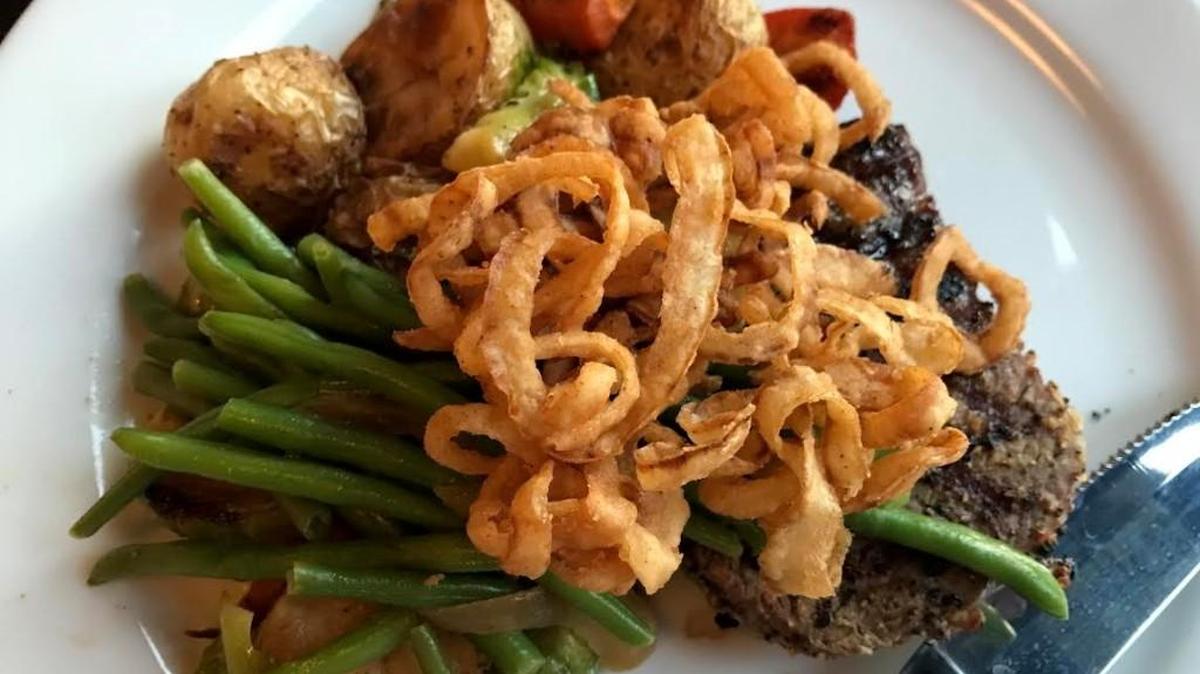 The black Angus filet at Two Olives is topped with french-fried onions and served with a side of roasted vegetables.