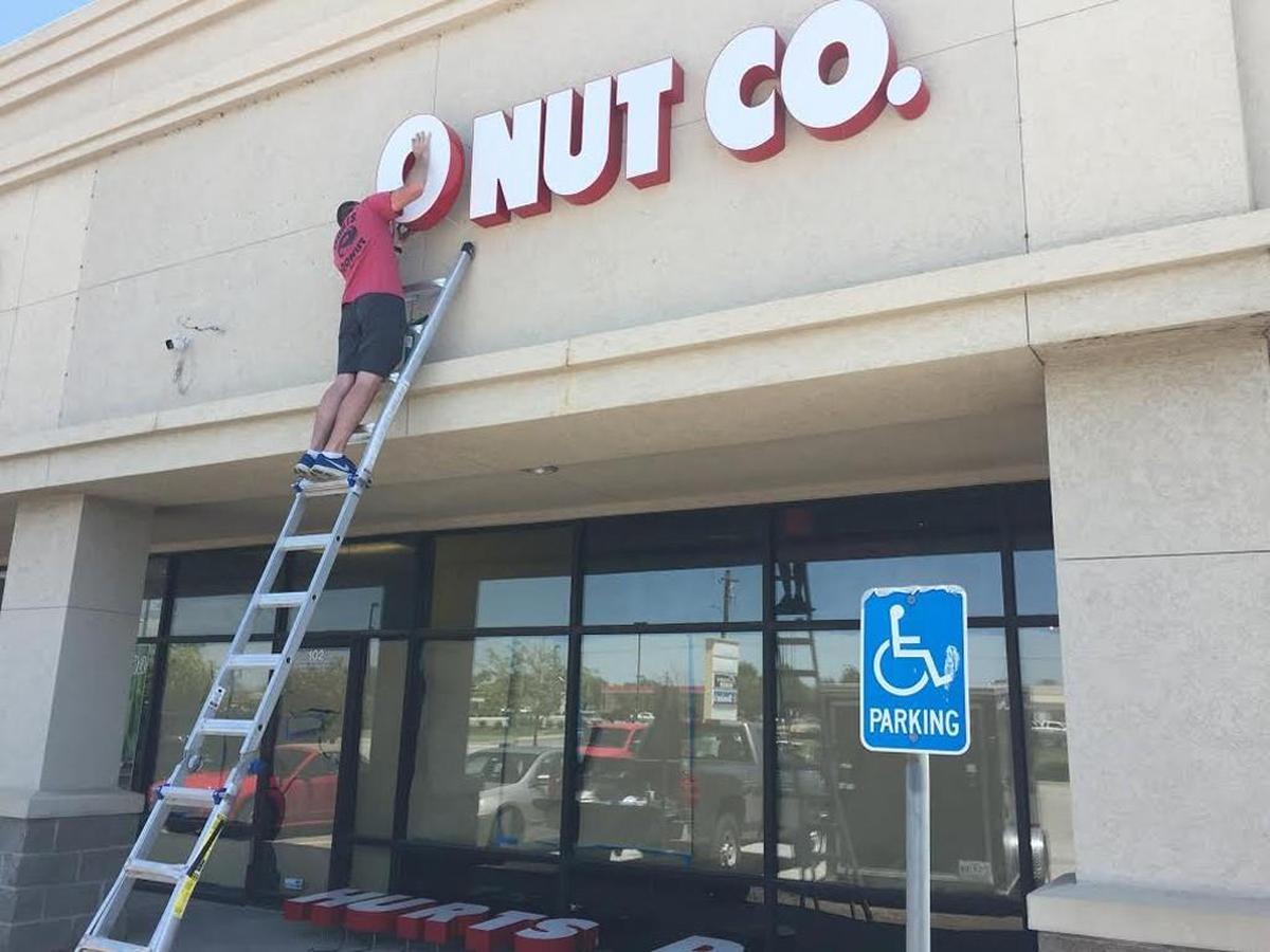 Workers hang the sign on the new Hurts Donut store near 37th and Woodlawn on Monday.