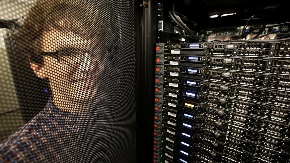 Massachusetts Institute of Technology researcher Carl Vondrick looks through a protective door while standing next to a computer server cluster, right, on the MIT campus, in Cambridge, Mass.