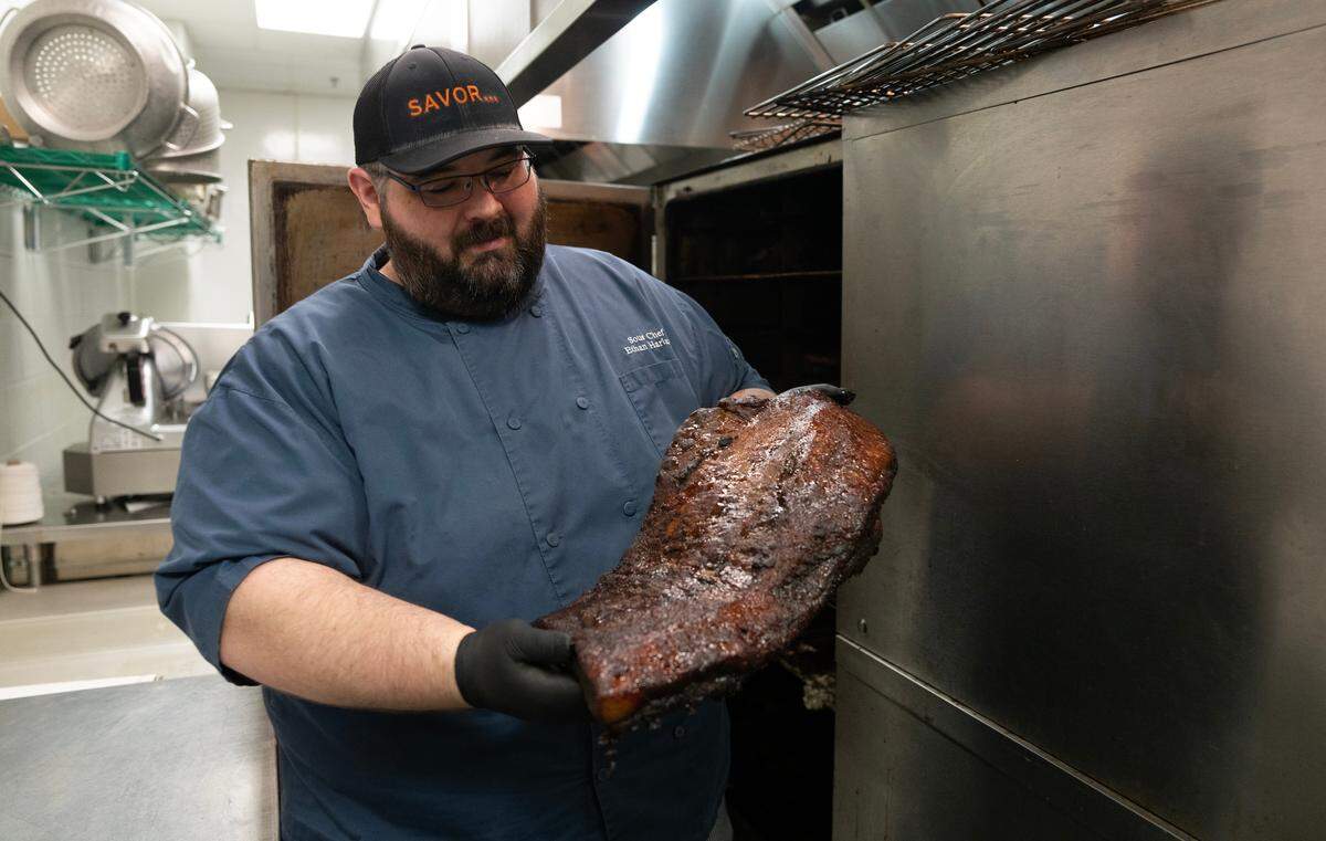 Ethan Harland, executive sous chef at INTRUST Bank Arena, pulls a brisket from the smoker. His staff will smoke 800 pounds of brisket and pork to prepare to feed 45,000 people for the NCAA Basketball Tournament.