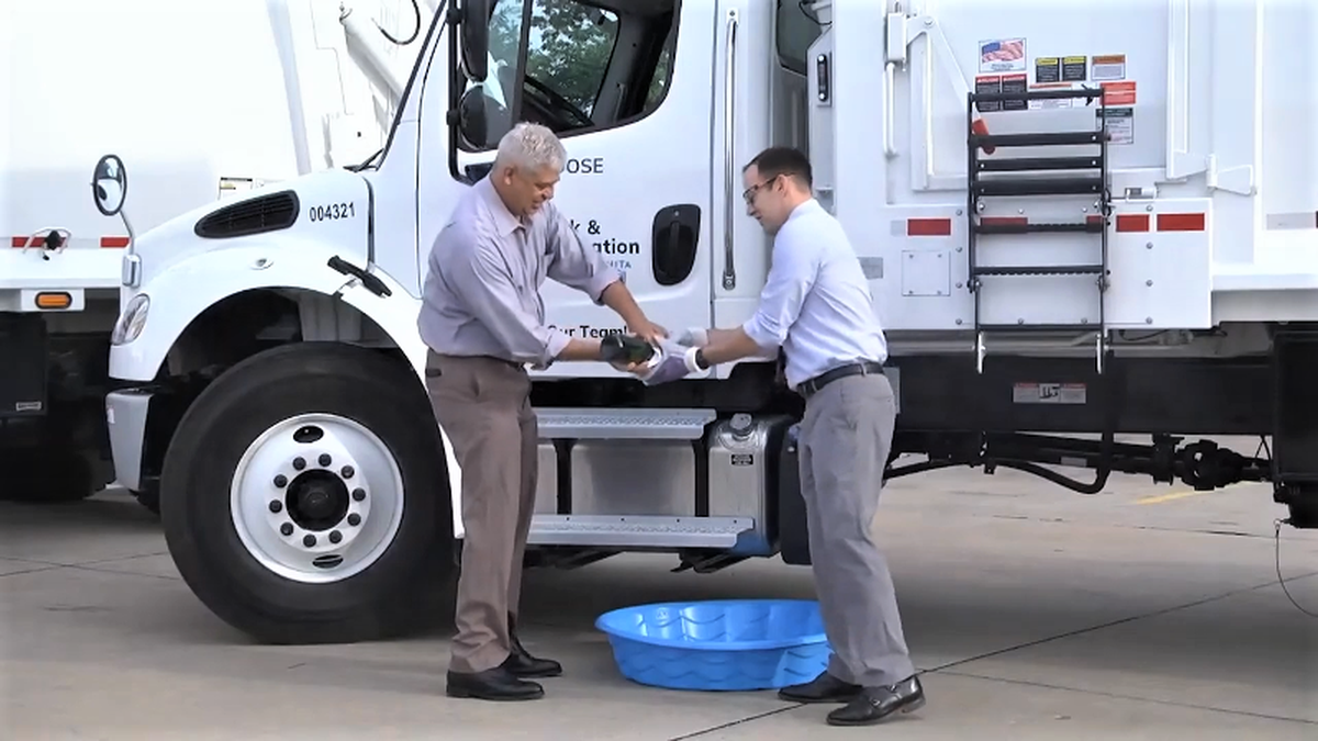 Parks director Troy Houtman hands Wichita Mayor Brandon Whipple the bottle to christen the first of two new trash trucks on Friday morning.