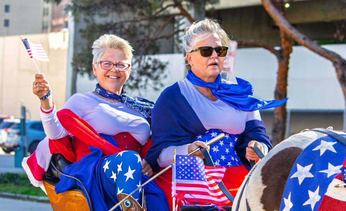 From the back of a horse-drawn carriage, a woman waves an American flag while riding in Wichita’s 2025 Veterans Day parade.