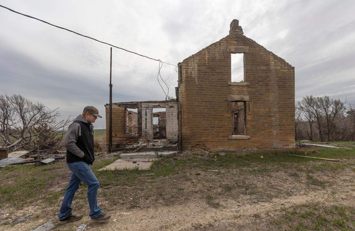 Grady Dickerson’s walks past a burned up homestead house near his family’s ranch near Paradise, Kansas.