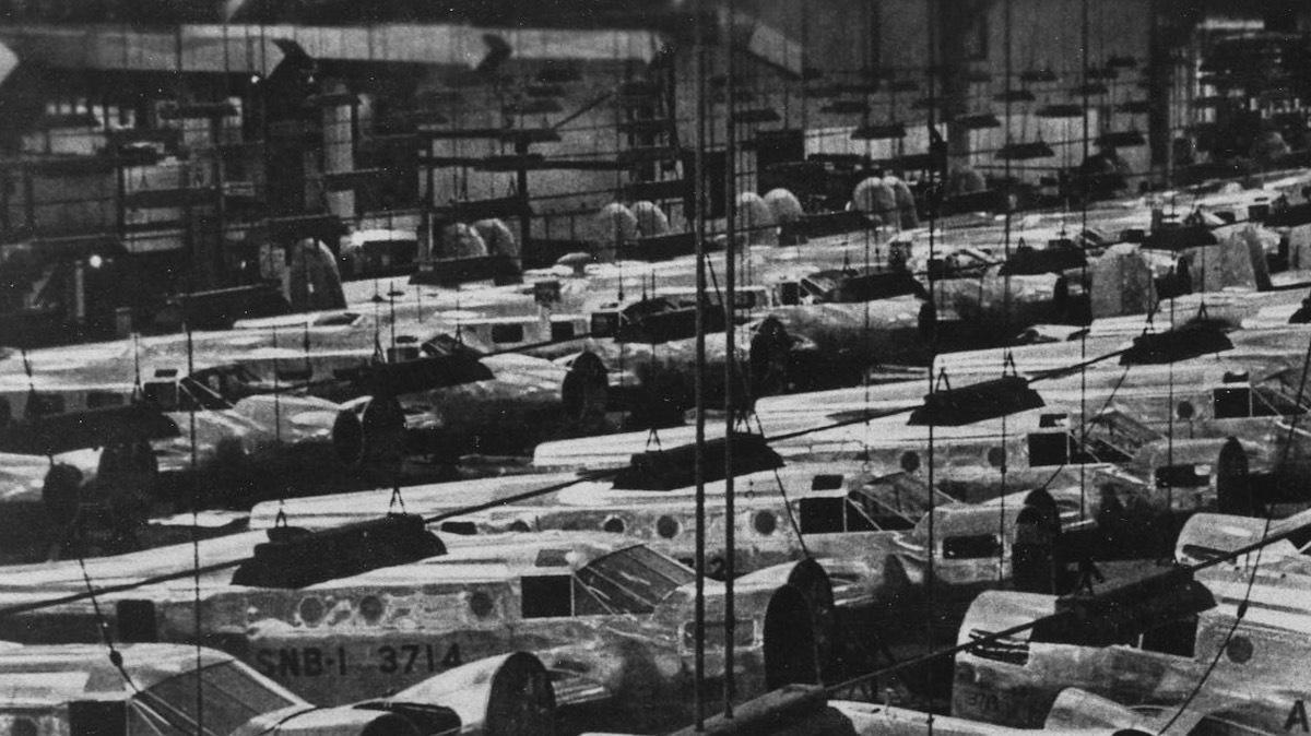 Walter and Olive Ann Beech look out over the wartime production line that almost overflows with airplanes. The photograph apparently used mirrors to make the factory output look even more daunting to any Axis spy who might happen upon it.