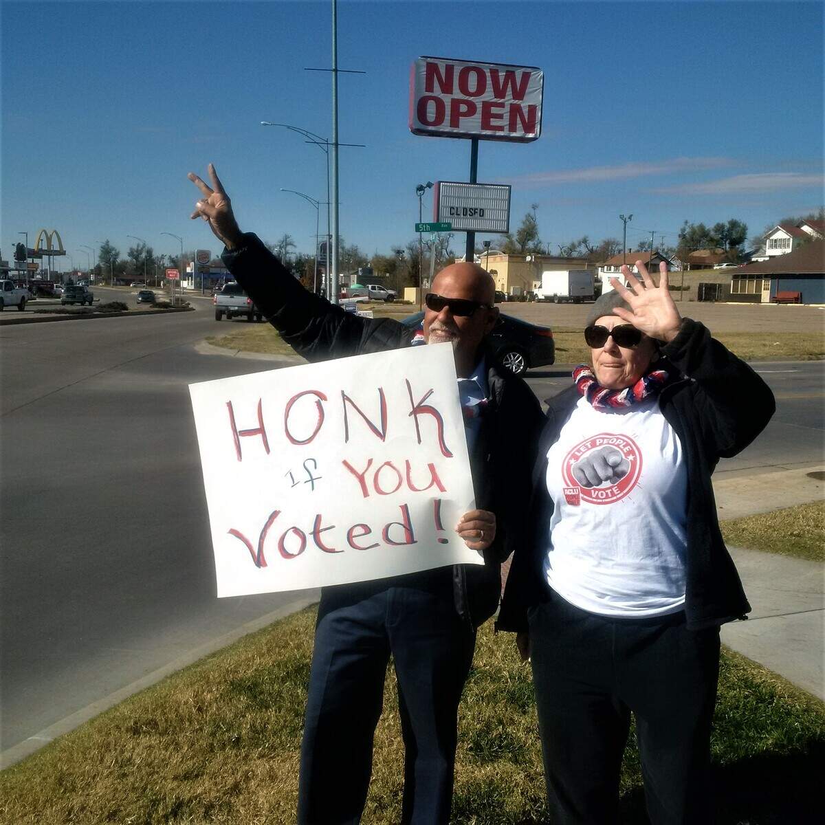 Rene Lopez of San Diego and Malley Sisson of Manhattan wave a sign to encourage voters in Dodge City.