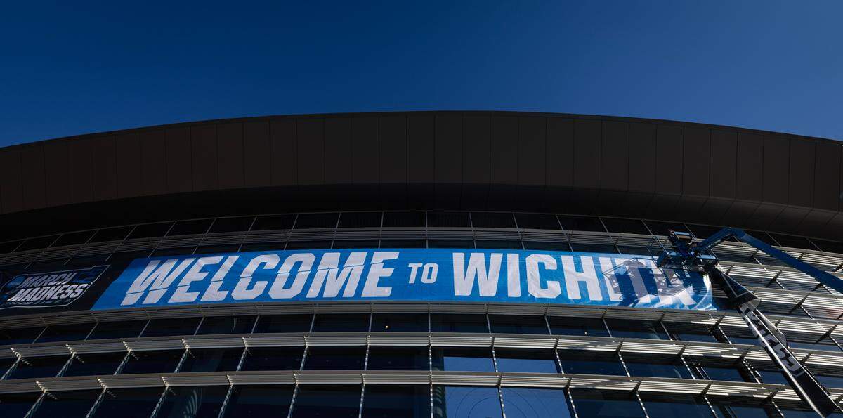 Workers hang a banner outside of Intrust Bank Arena on Sunday morning welcoming fans to the NCAA Tournament. 