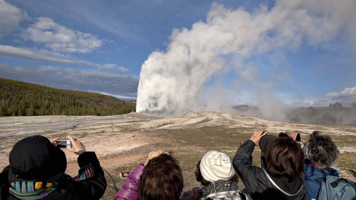 In this May 21, 2011, file photo, tourists photograph Old Faithful erupting on schedule late in the afternoon in Yellowstone National Park, Wyo. Yellowstone National Park officials say they’ve ticketed a man caught on video walking dangerously close to Old Faithful geyser.
