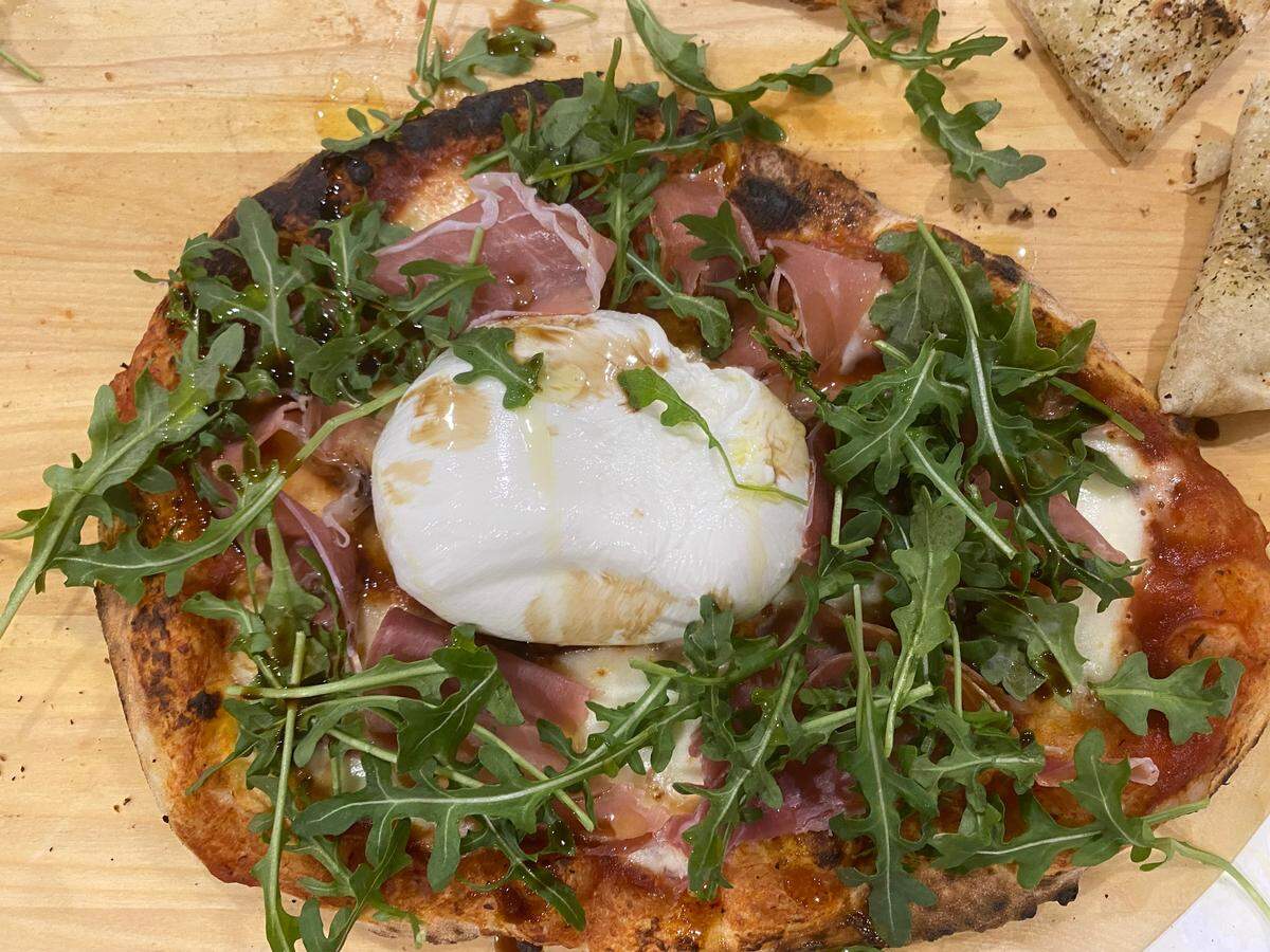 A pizza cooked in a gas-powered Ooni pizza oven on Piatto dough then topped with burrata, prosciutto, arugula and a drizzle of olive oil and balsamic vinegar