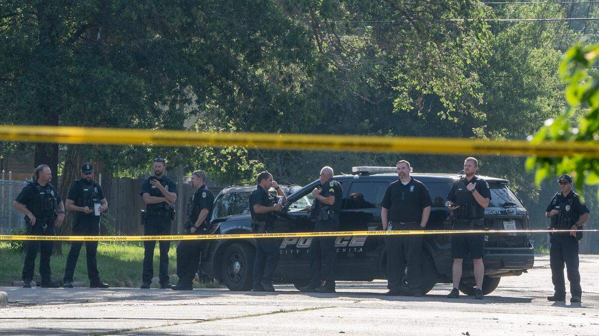 Wichita police officers wait while a police dog works in Skyline Park on Tuesday morning. The police presence was in connection to a 14-year-old being fatally shot. Three teens have been arrested.