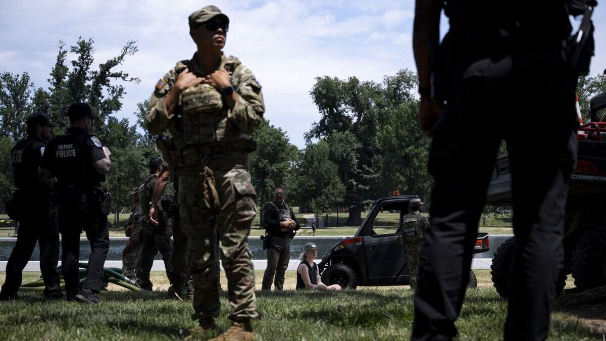 A young woman sits on the grass as she is detained before being issued a ticket after allegedly reaching into the reflecting pool and removing a piece of the coating that has peeled off at the Lincoln Memorial Reflecting Pool following the completion of recent renovations in Washington, DC, on June 22, 2026. US President Donald Trump on Monday threatened jail time for anyone seeking to damage one of his signature renovation projects, the Reflecting Pool at the Lincoln Memorial in Washington, whose overhaul has become a political flashpoint. Trump brought in contractors to drain the 610-meter pool and repaint it "American flag blue." But soon after completion of the work the coating has begun to peel off and algae turned the pool's water a mucky green -- setbacks the president blamed on vandals, without providing evidence. (Photo by Kent Nishimura / AFP via Getty Images)