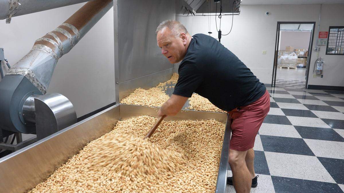 Nifty Nuthouse owner Steve Jahn pushes 150 pounds of cashews onto the drying table after he roasted them.