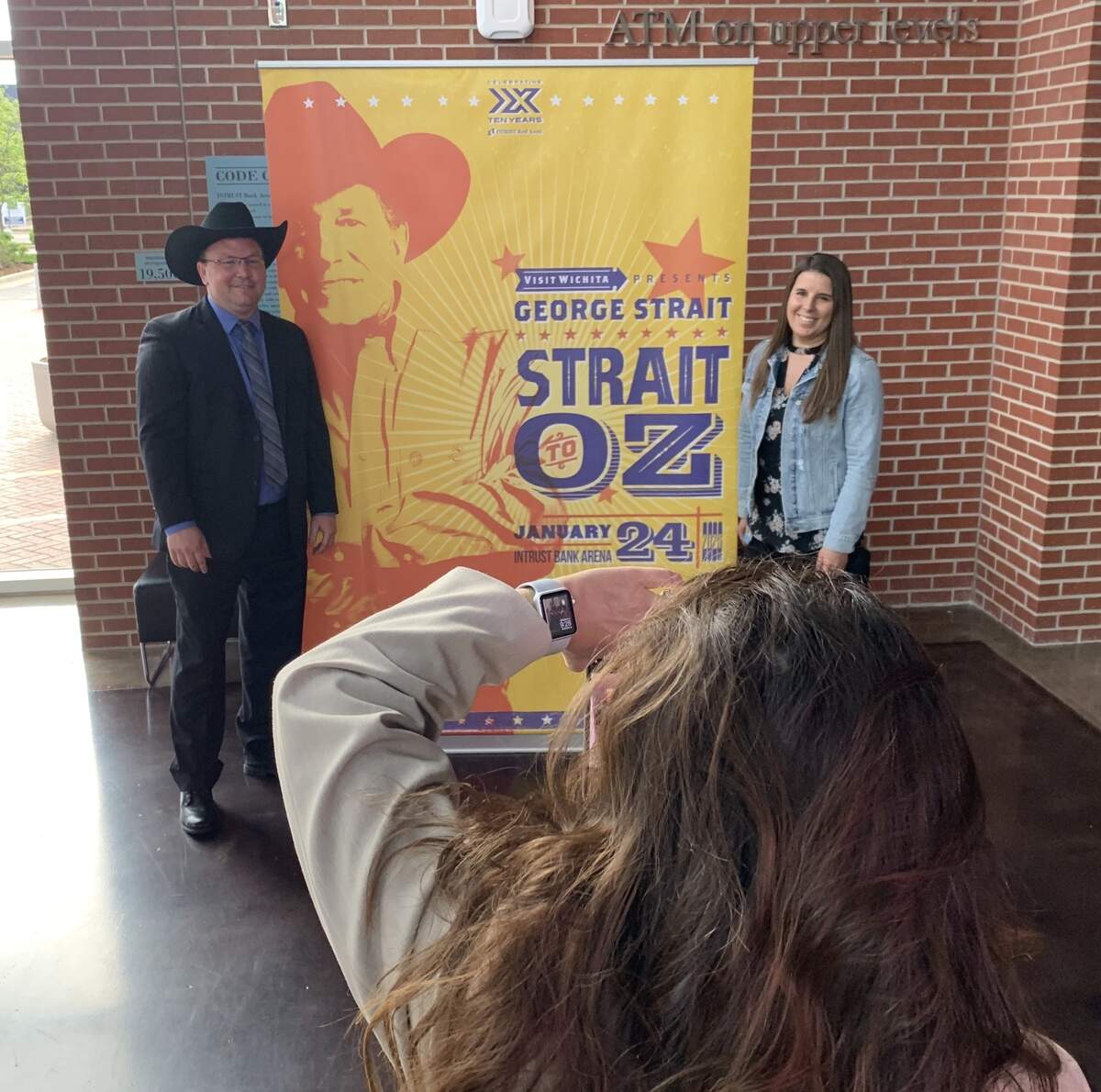 Intrust Bank Arena’s general manager A.J. Boleski and director of booking and marketing Christine Pileckas pose in front of a billboard announcing next year’s concert by George Strait.