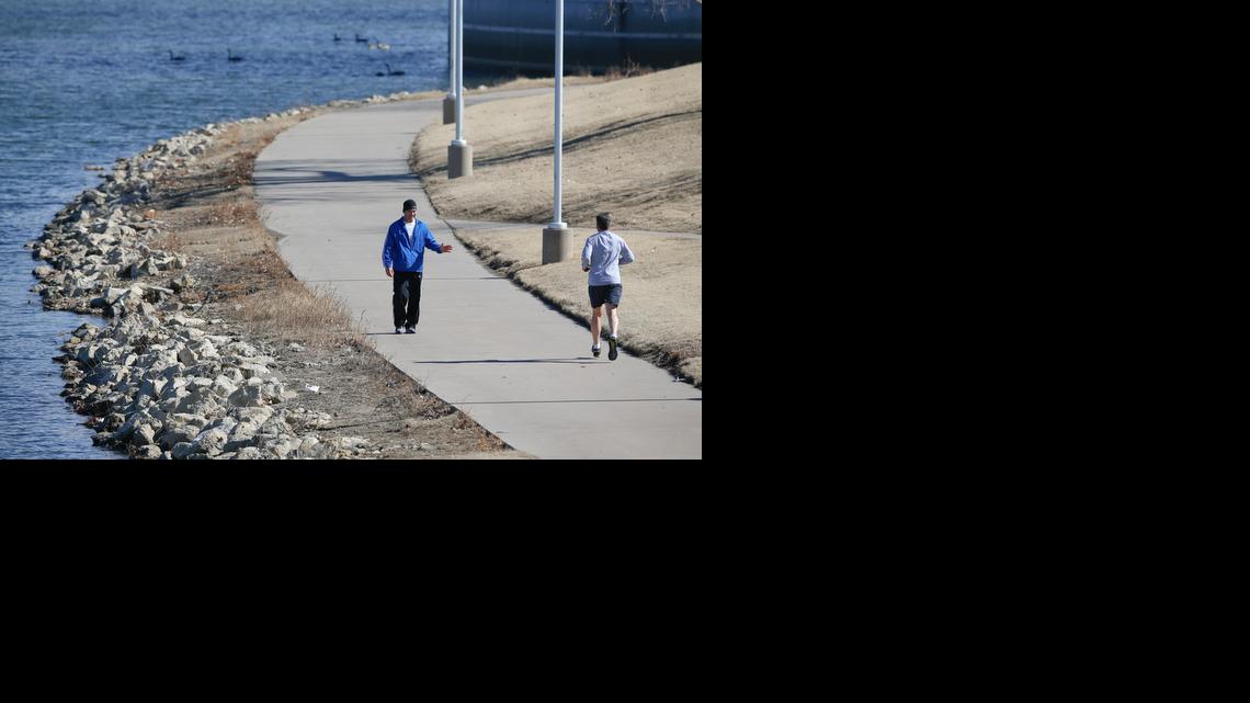 A walker waves to a runner along the Arkansas River near Exploration Place. A Wichita Pedestrian Master Plan is in the works.

