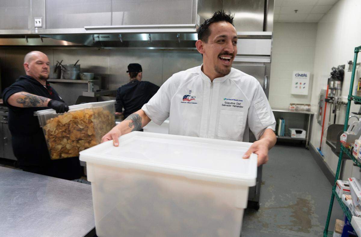 Salvador Hernandez, executive chef at INTRUST Bank Arena carries potato chips that were made by his staff in preparation for the NCAA Basketball Tournament. At far left is Farley Charwell.