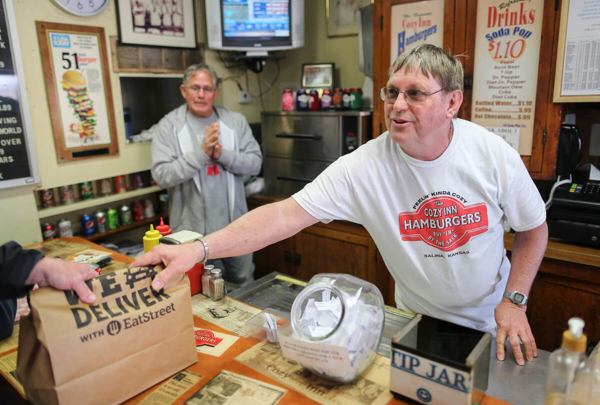 Terry Shank hands over a bag of hamburger sliders to a customer at the Cozy Inn in Salina on Tuesday. The famous Kansas hamburger stand will celebrate their 100th anniversary this weekend.