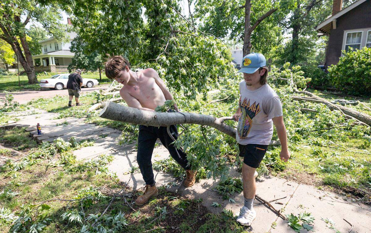 Titan Claussen, left, and Jason Ratzlaff remove fallen tree limbs from Ratzlaff’s yard in Halstead on Monday. The town suffered extensive damage from a storm that passed through on Sunday night.