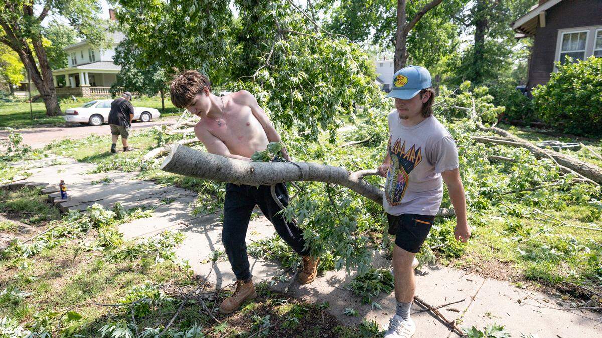 Titan Claussen, left, and Jason Ratzlaff remove fallen tree limbs from Ratzlaff’s yard in Halstead on Monday. The town suffered extensive damage from a storm that passed through on Sunday night.