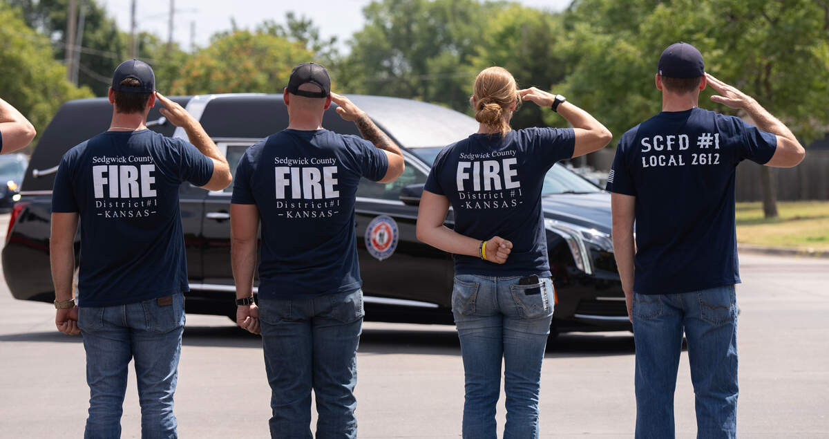 Sedgwick County Firefighters salute the hearse carrying Ty Voth as it turns at Maple and 119th St. W. Voth collapsed and died suddenly while working on a house fire Thursday afternoon,