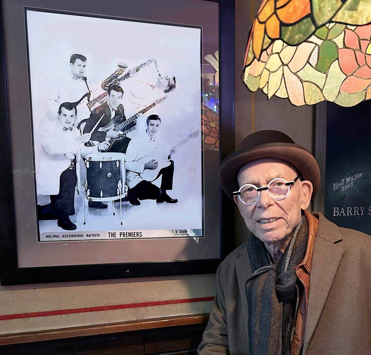 An older Bucky Walters in front of a photo of his band, the Premiers, in which a young Bucky Walters was the lead singer.