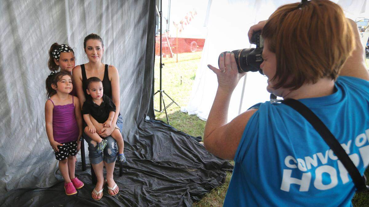 Photographer Robin Cowell takes a free family portrait during the 2015 Convoy of Hope. Thousands are expected to show up to receive free backpacks, shoes for children, haircuts, family portraits and other services Saturday, Aug. 4.