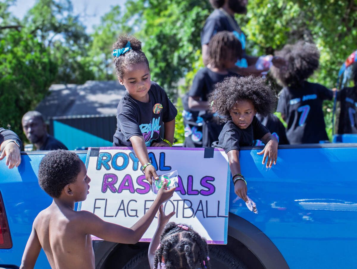 Kids pass out goodie bags from a truck bed during parade.
