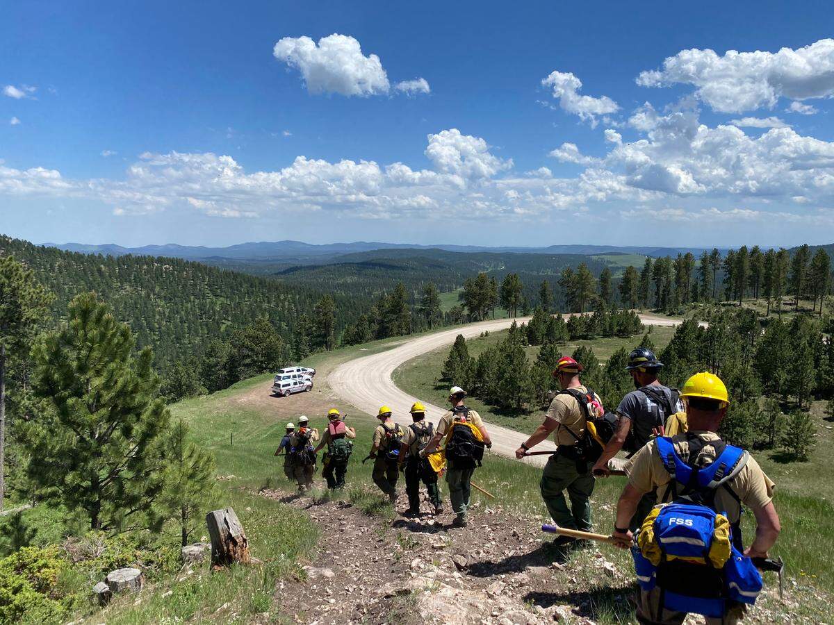 A 10 person hand crew called a “suppression module” from Kansas walks downhill after fighting fires this summer outside of Custer, South Dakota. Suppression modules fight fire by just using hand tools. In this photo: Chris Hanson, Bryce Haverkamp, Chris Hanson Sr., Aaron Kirby, Matt Miller, Chris Talmadge, Josh Ward, Bailey Penner, Austin Gilliam and Phil Lierz.