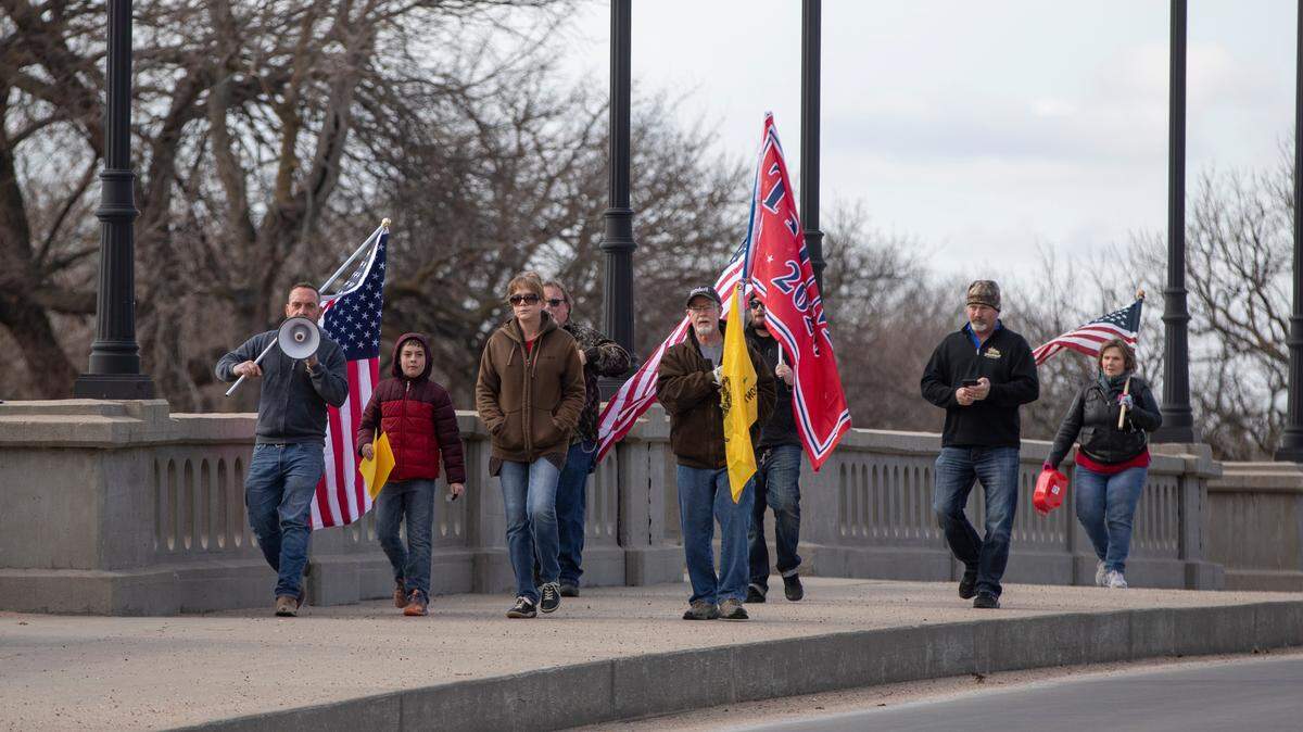 A small group of protesters walk across a bridge at Central Riverside Park as they march to the Sedgwick County Courthouse on Wednesday for a “Stop the Steal” rally on the courthouse plaza.