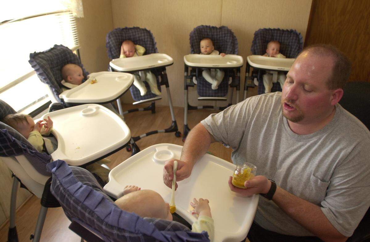 Eldon Headrick feeds his 1-year-old son, Sean, in 2003, while the five other babies wait for their mother to return with more food for them.