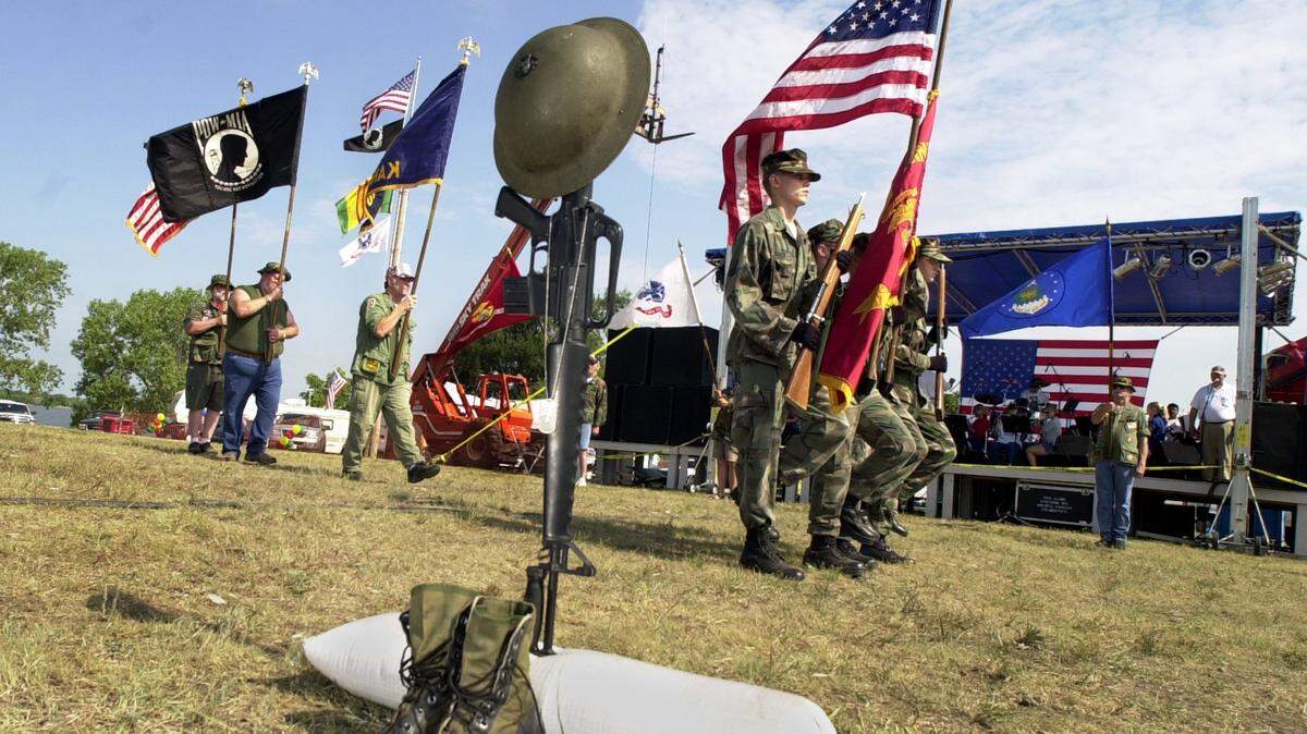Members of the color guard and a member of each service branch walk past a  marker representing a fallen soldier during
activities at the Kansas Vietnam Veterans and Family Reunion at El Dorado Lake in 2013.