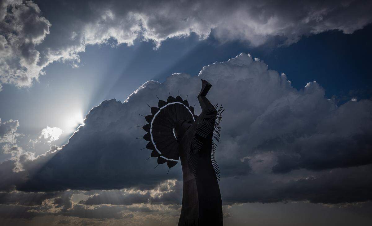 The Keeper of the Plains before a canvas of sun rays and clouds.