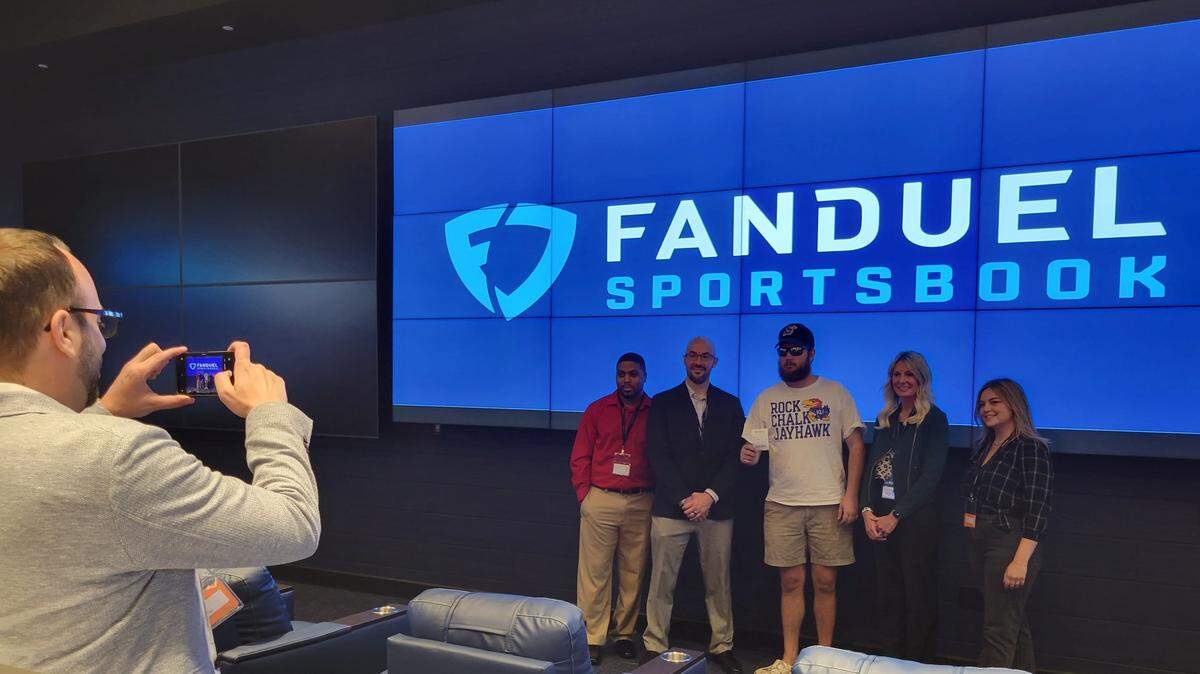Chuck Bass holds up his ticket as he poses for a photo with casino and FanDuel officials at the Kansas Star Casino on Thursday. He was one of the first people to legally bet on sports in the state.