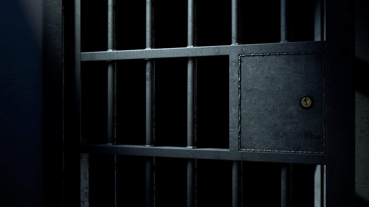 A closeup of the locking mechanism of an open jail cell with welded iron bars on a dimly lit dark background