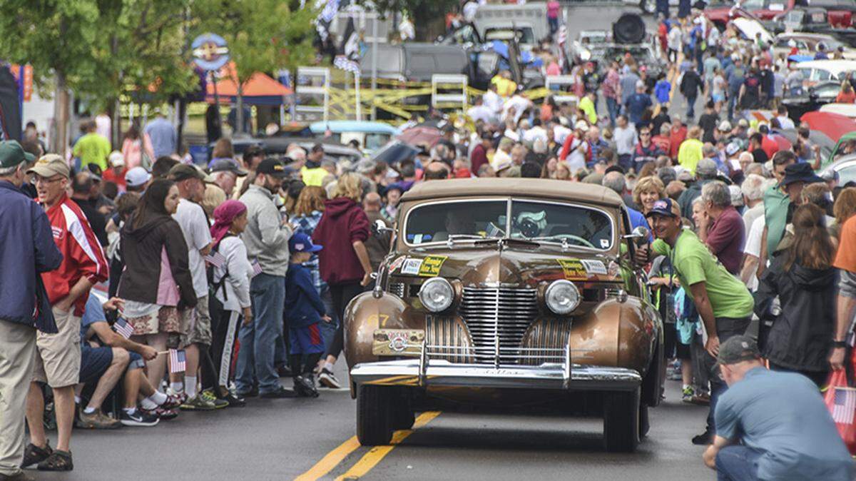 Spectators gather around a city street as cars participating in the Great Race start to roll into Fairport, New York in 2018.