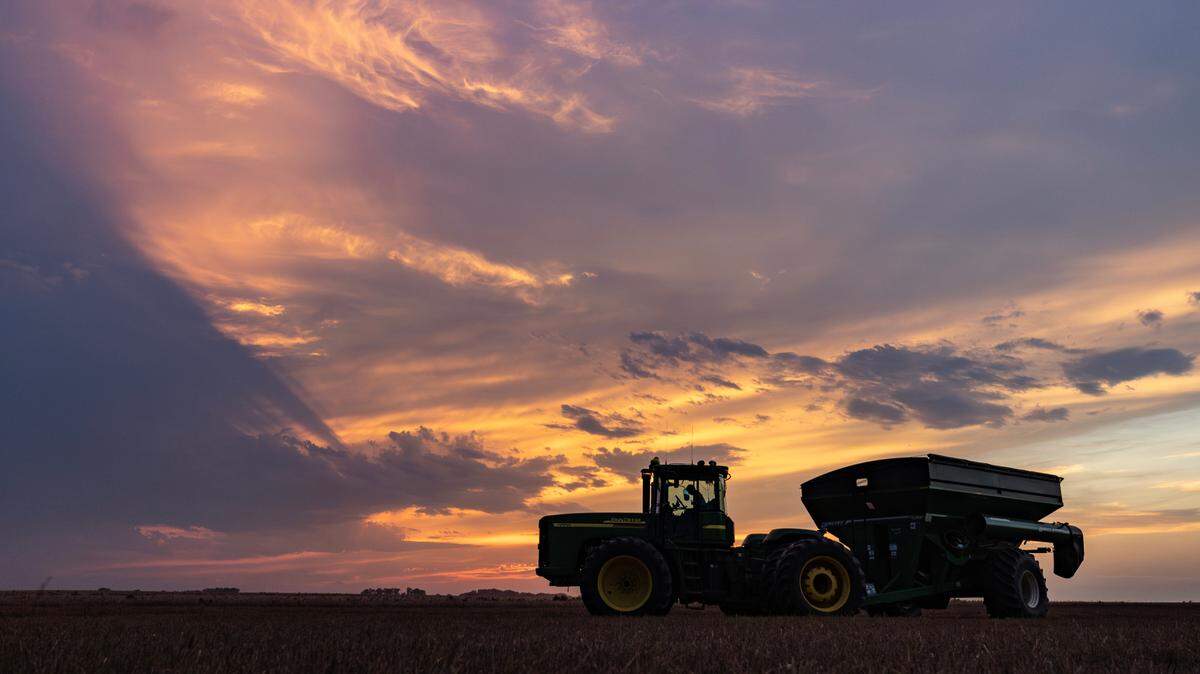 A tractor and grain cart wait for a load of wheat just after sunset in a Reno County wheat field in 2023.