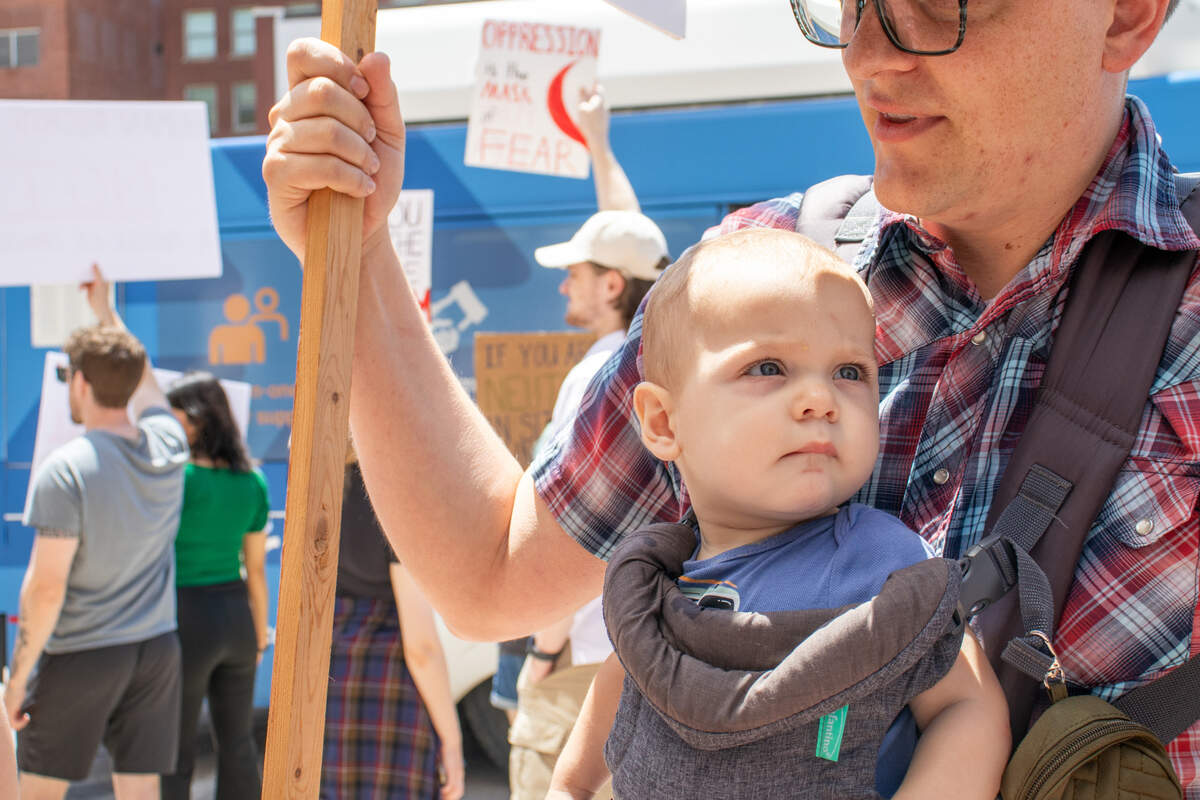 A father holds a protest sign while protesting at the “No Kings” demonstration with his wife and young son. It was the family’s first protest.