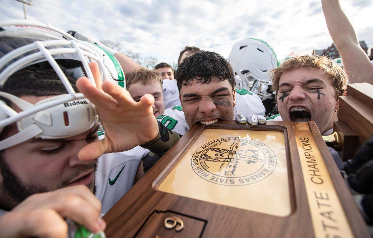 Derby football players sink their teeth into the 6A state championship trophy after defeating Olathe North 63-26 on Saturday in Emporia.