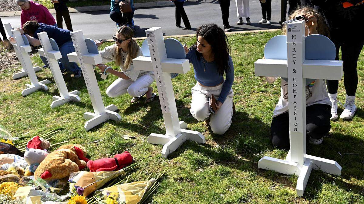 People gather to sign wooden crosses placed at a makeshift memorial by the entrance of the Covenant School on Tuesday, March 28, 2023, in Nashville, Tenn. Three children and three school staff members were killed by a former student in Monday’s mass shooting.