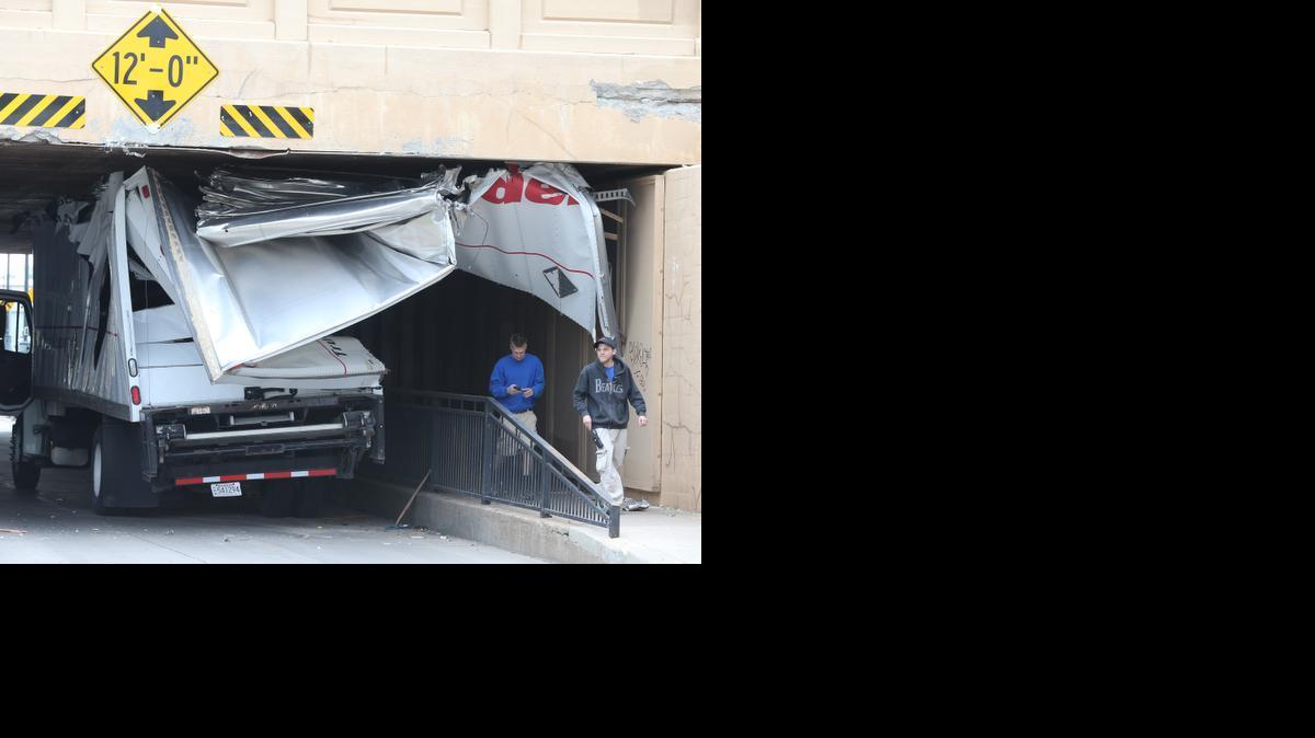 Pedestrians walk by the shredded remains of a Ryder Rental truck Friday morning on Waterman near Intrust Arena. The truck, much taller than the 12-foot railroad bridge, became wedged in the eastbound lane after shearing off its roof. (May 16, 2014)


