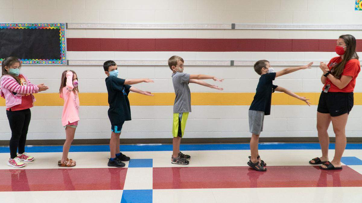 Masked students at Apollo Elementary School do “the shark” with their hands to remind them to keep their distance from each other.