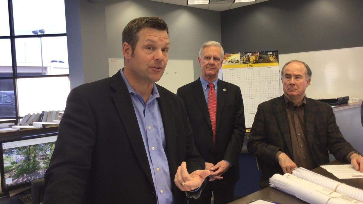 Kris Kobach talks about taxes, as running mate Wink Hartman and longtime Republican activist Bob Dool look on.