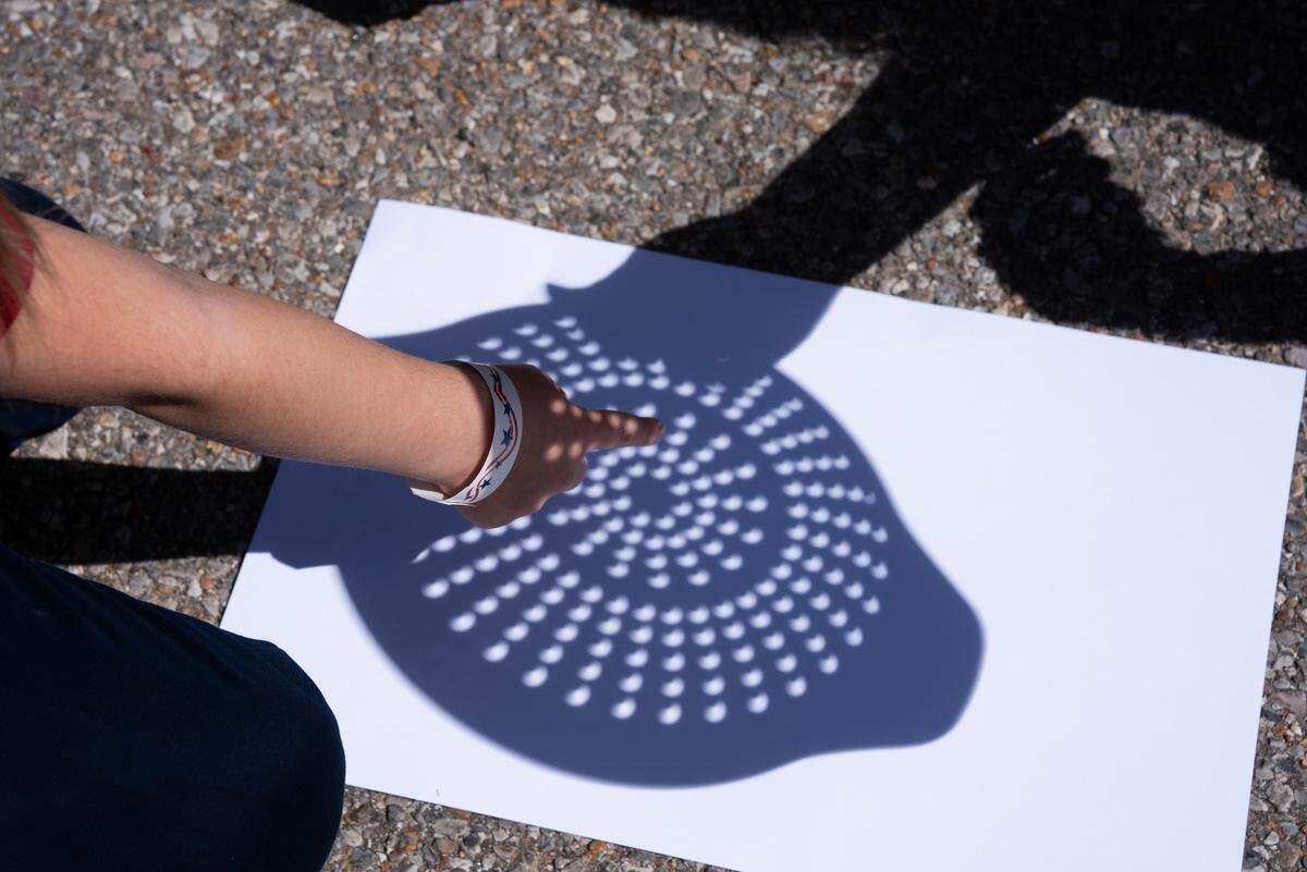 Selena Steele Denny points at the shape made from a colander her mother is holding during an eclipse party at Exploration Place on Monday.