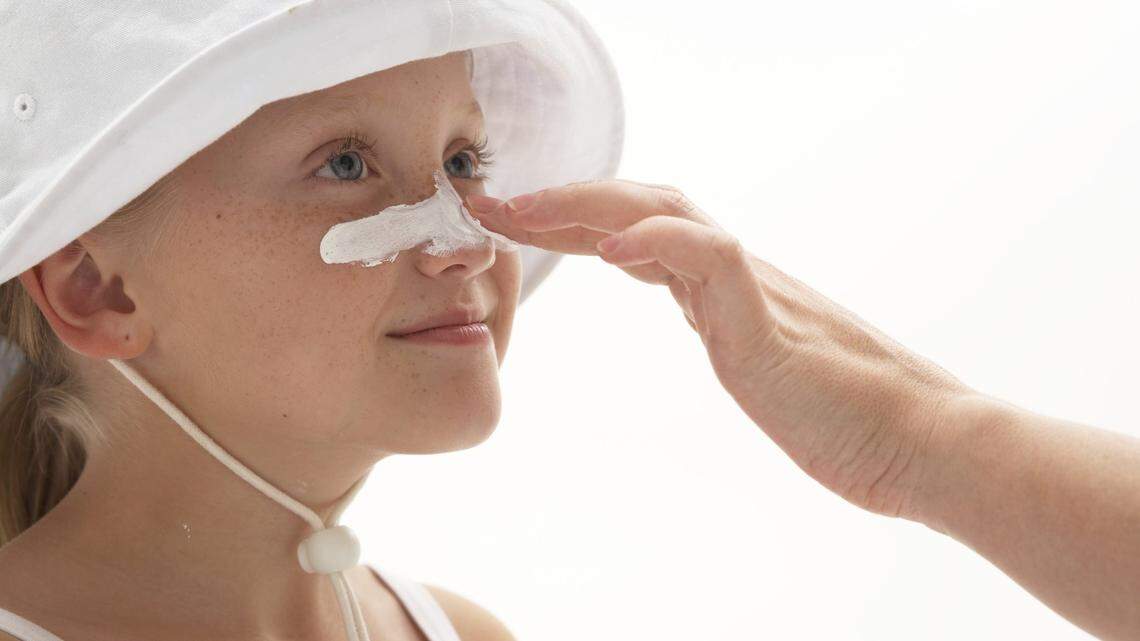 Girl (7-9) having sun cream applied to nose