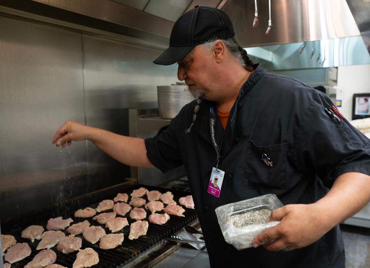 Herman Veley seasons chicken breasts in the kitchen at INTRUST Bank Arena in preparation for the NCAA Basketball Tournament.
