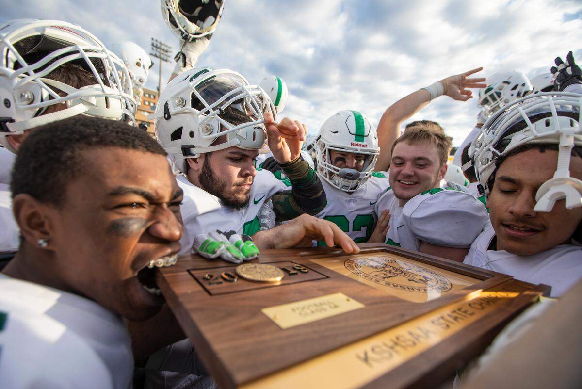 Derby football players sink their teeth into the 6A state championship trophy after defeating Olathe North 63-26 on Saturday in Emporia.