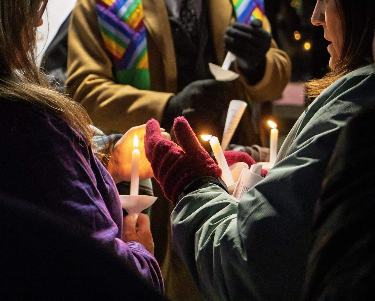 Worshipers share a candle's flame during an ecumenical public worship service Sunday outside the Wichita office of the Department of Homeland Security, where they gathered to pray, sing songs and protest after the killing of Renee Good.