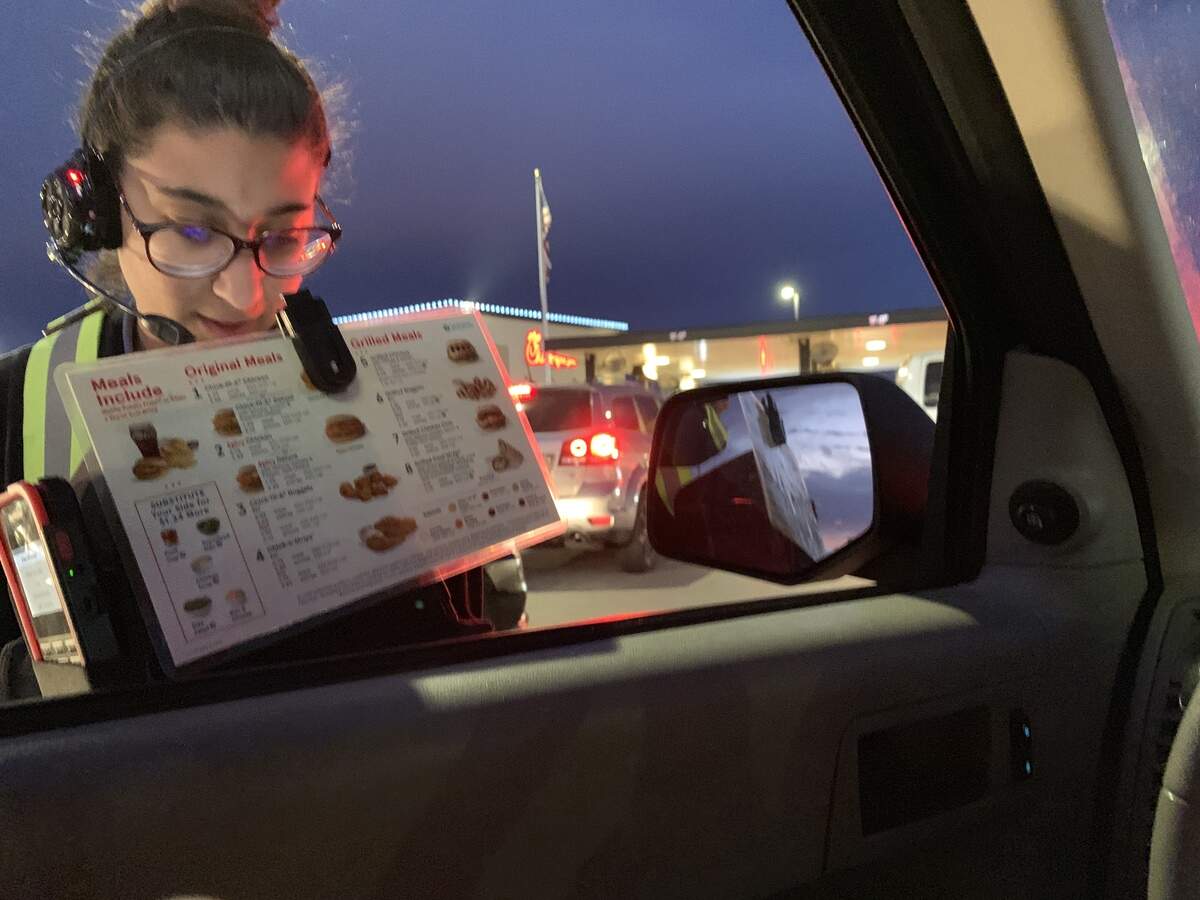 A Chick-fil-A employee takes an order at a car window.